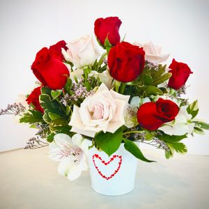 One dozen mixed pink and red roses with accent, filler, and greens in heart container